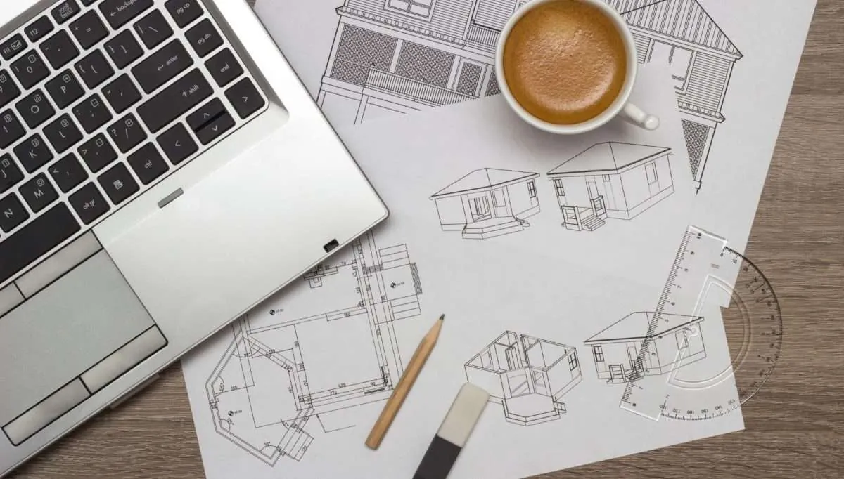 Notebook, xícara de café e plantas técnicas sobre mesa de trabalho